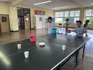 卓球のピンポン玉をラケットで打ち、紙コップなどの容器に入れるゲームを楽しむ様子