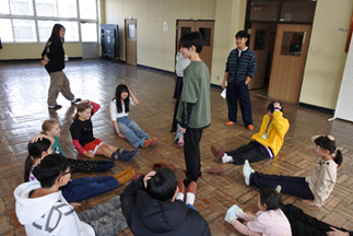 R7年新年子ども会のリーダーさがし（円陣を組み、一人リーダーを決め、他の人がリーダーのジェスチャーをまね、円陣の中に人が入り、誰がリーダーかを当てるゲーム）を楽しむ様子